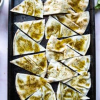 pita bread cut into wedges over a baking tray, brushed with zaatar olive oil and ready to bake for chips