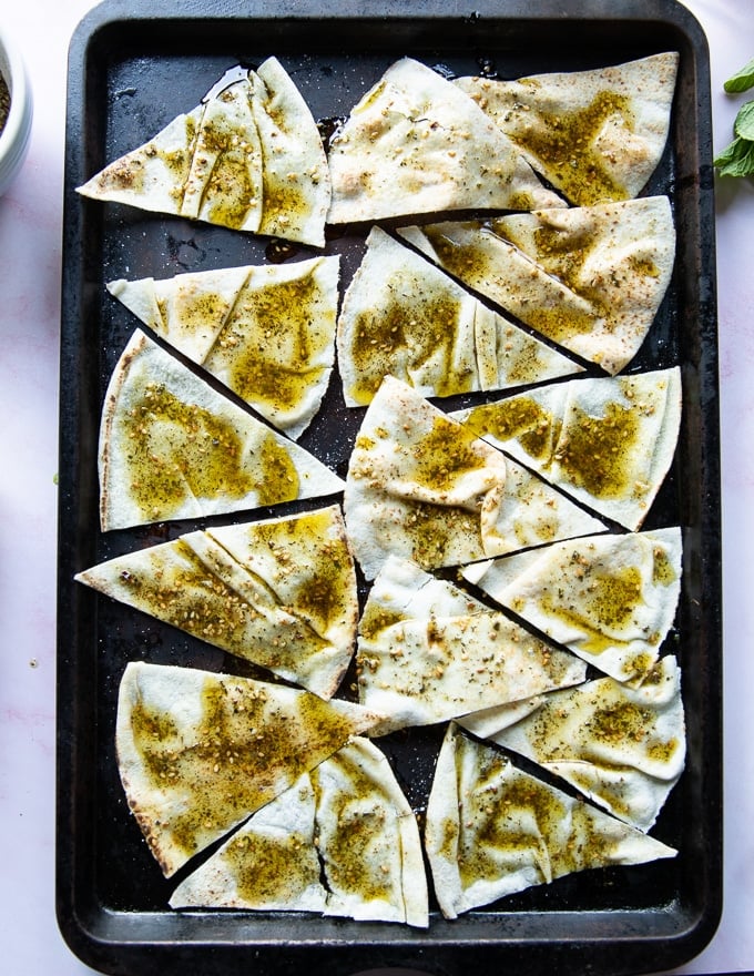 pita bread cut into wedges over a baking tray, brushed with zaatar olive oil and ready to bake for chips