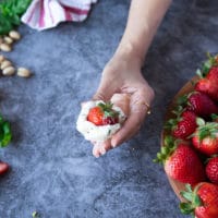 A hand rolling the goat cheese over the strawberries