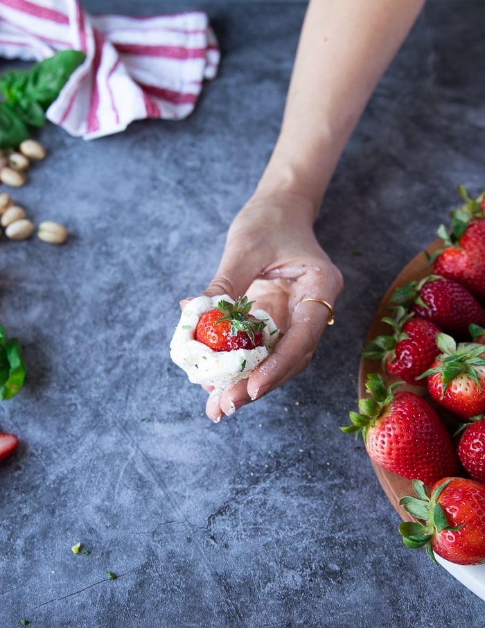 A hand rolling the goat cheese over the strawberries 