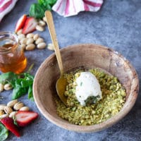 The goat cheese strawberry in the bowl of pistachios and a spoon rolling it