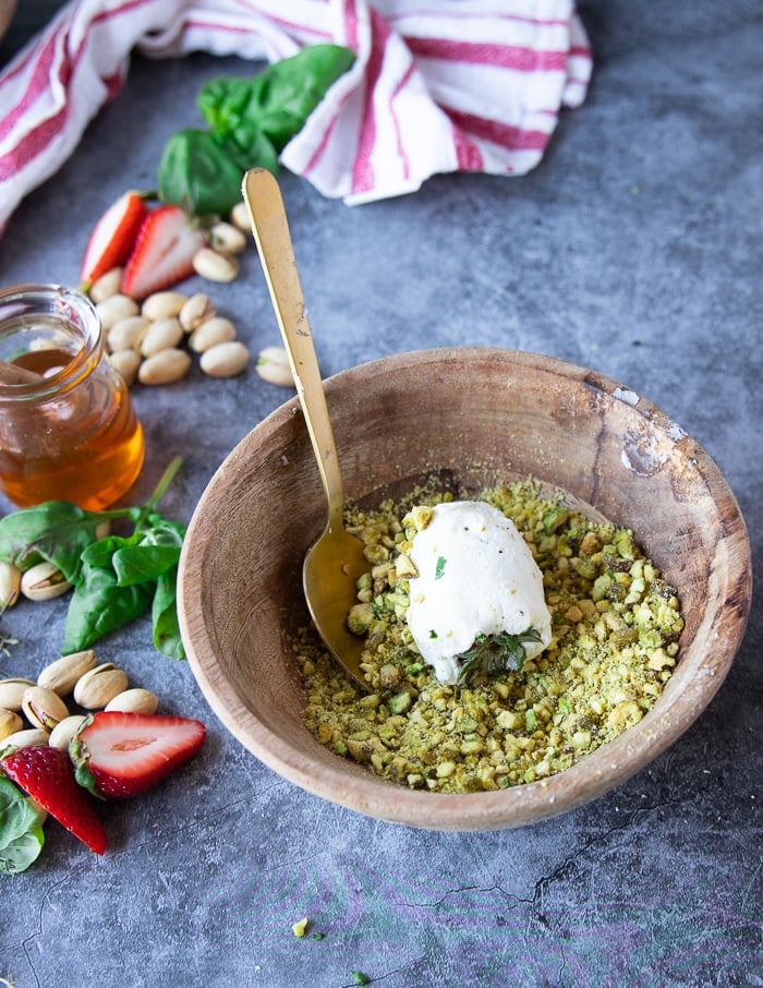 The goat cheese strawberry in the bowl of pistachios and a spoon rolling it