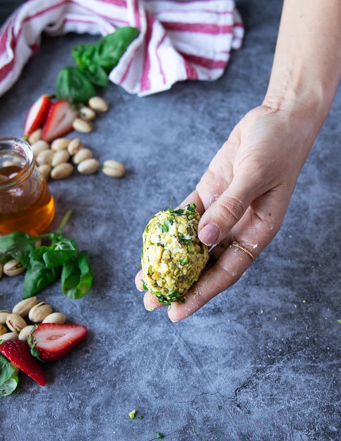 A hand holding the strawberries coated in pistachios