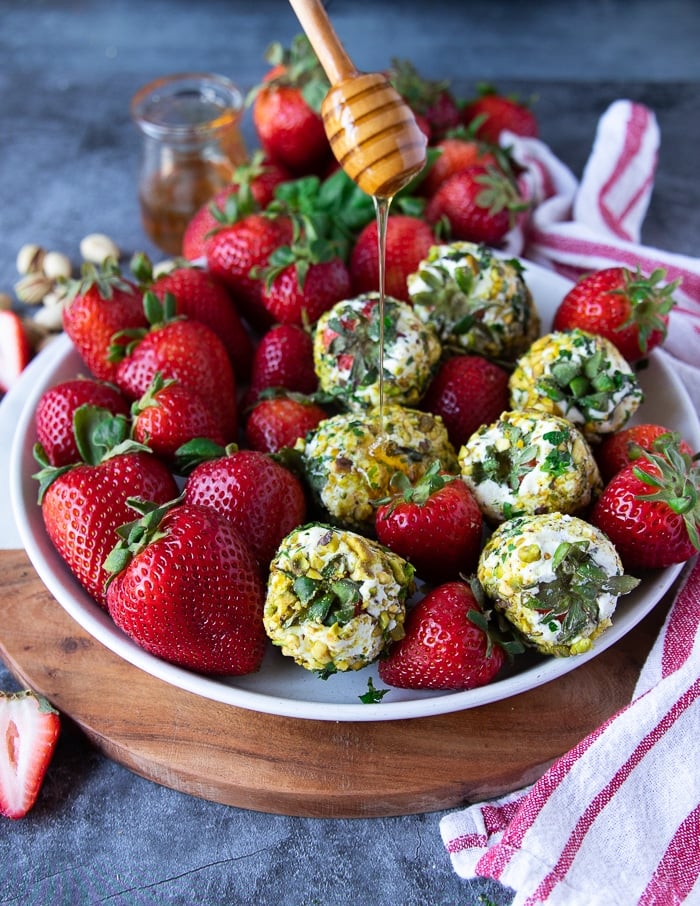 a plate of goat cheese appetizer with fresh strawberries and a hand drizzling honey over them 