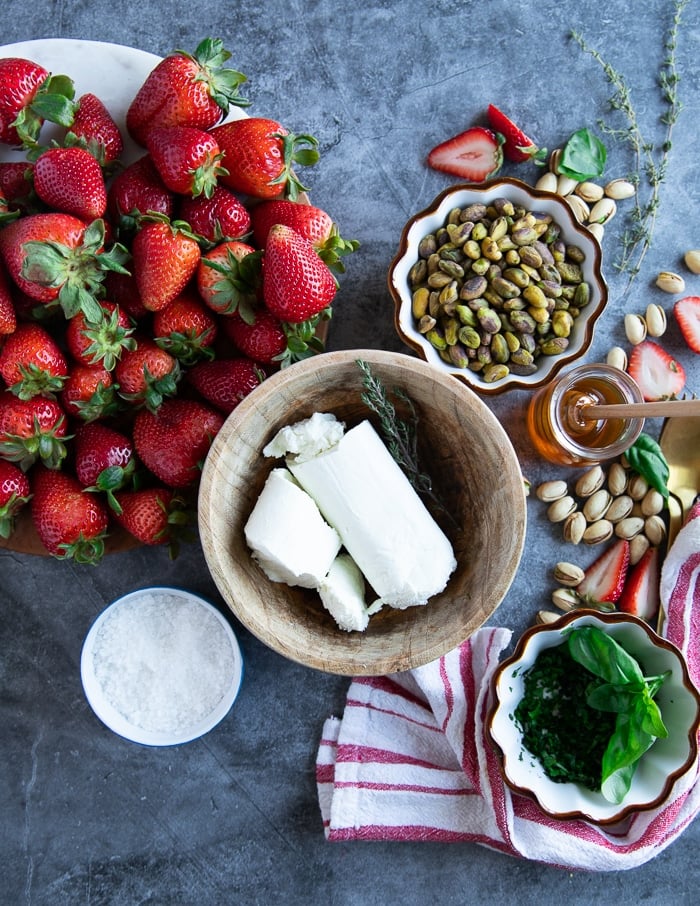 Zutaten für eine Ziegenkäse-Vorspeise, darunter eine Schüssel Ziegenkäse, eine Schüssel Pistazien, Basilikum und viele frische Erdbeeren