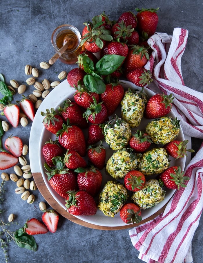 A full plate of goat cheese appetizer with strawberries and extra berries on the side, some fresh basil and pitsahcios