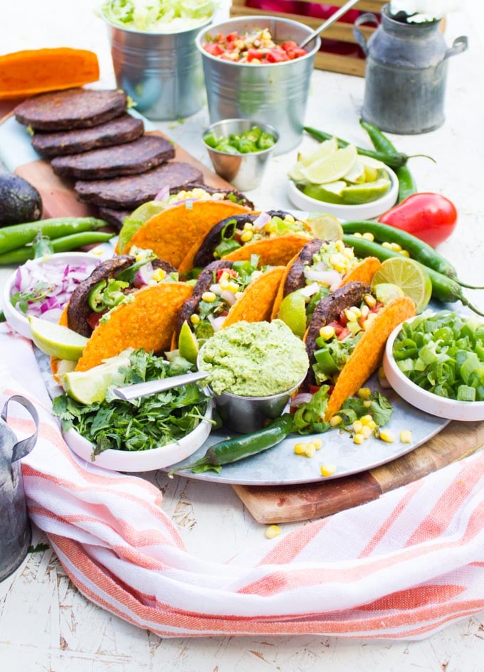 A burger taco party with all the ingredients taco shells, grilled burgers, guacamole, salsa, chopped jalapenos and chopped onions