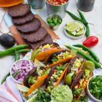 A tacos party set up with grilled burgers, assembled tacos, guacamole, salsa and fresh cilantro toppings