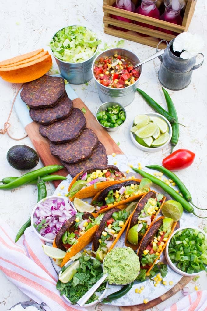 Top view of A burger taco party with all the ingredients taco shells, grilled burgers, guacamole, salsa, chopped jalapenos and chopped onions