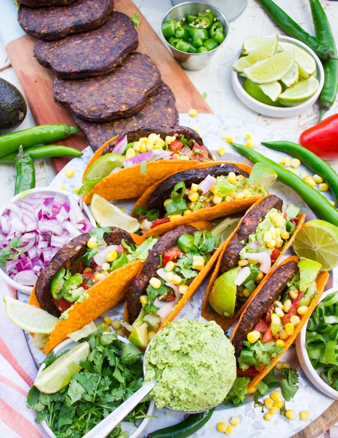 Close up view of the table A burger taco party with all the ingredients taco shells, grilled burgers, guacamole, salsa, chopped jalapenos and chopped onions