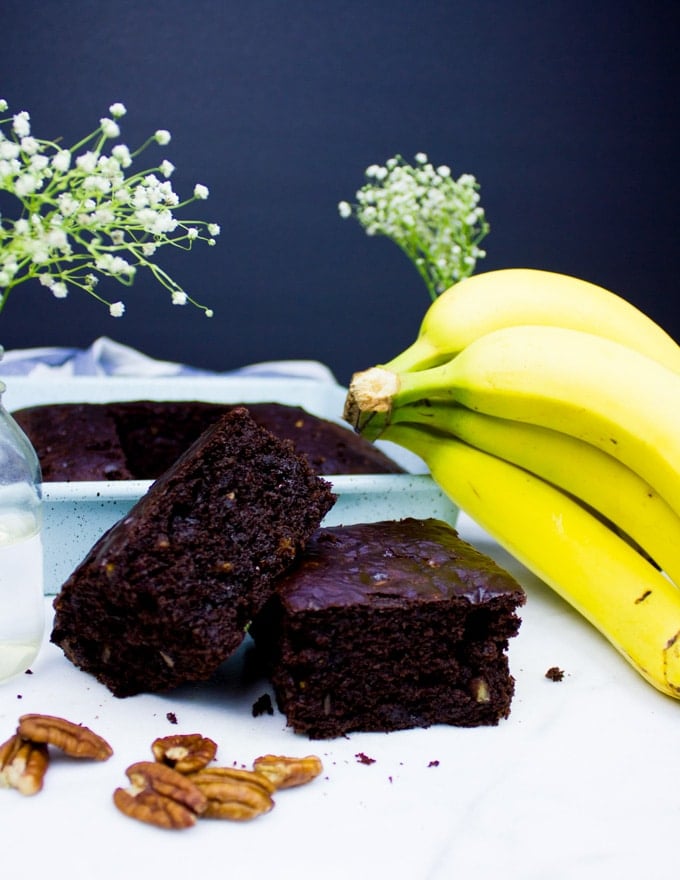 two slices of banana chocolate chip pieces on top of each other and a banana bunch near them.