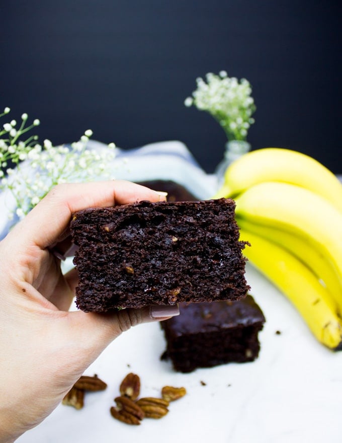 A hand holding close up a pice of chocolate banana bread or banana chocolate chip cake showing the fluffy texture.