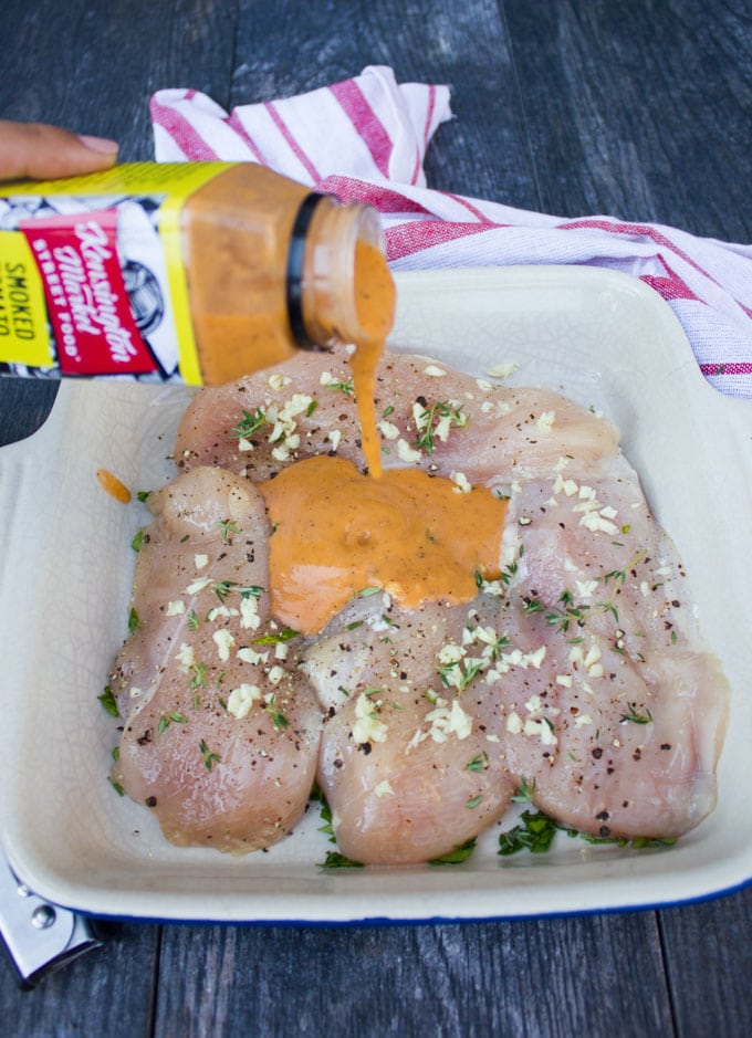 Pouring a tomato salad dressing to marinate the raw chicken breasts over a deep dish