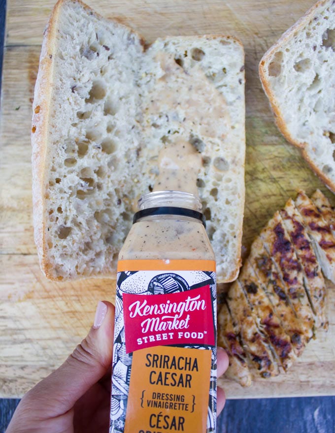 a hand pouring a sriracha salad dressing over a loaf of sandwich bread