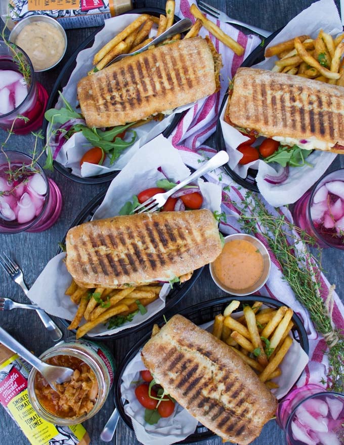 A top view table set up with four panini pressed sandwiches served with fries and some drinks on the side