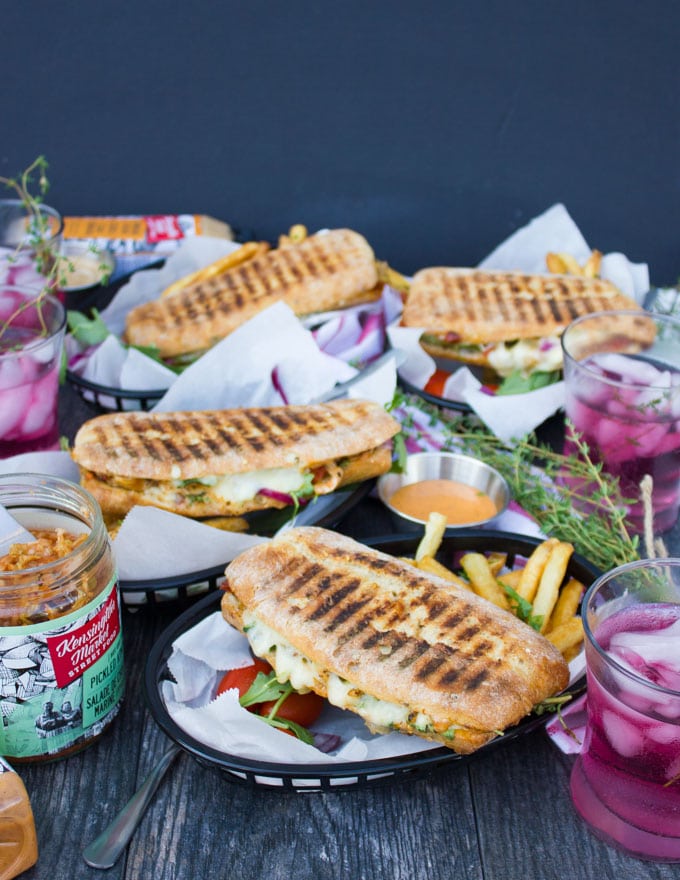 a side view showing a table set up with four panini pressed sandwiches served with fries and some drinks on the side