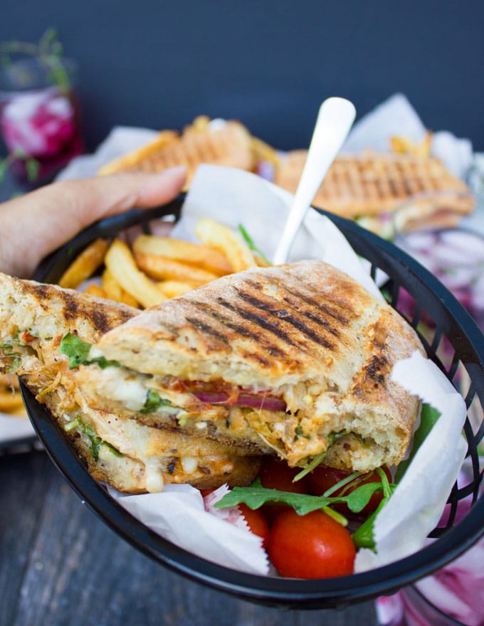 a hand carrying a plate of a split in half sandwich showing the filling of the sandwich 