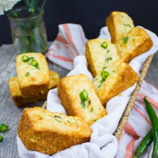 A basket with a few cornbread muffins and some spicy green chillies and a kitchen towel