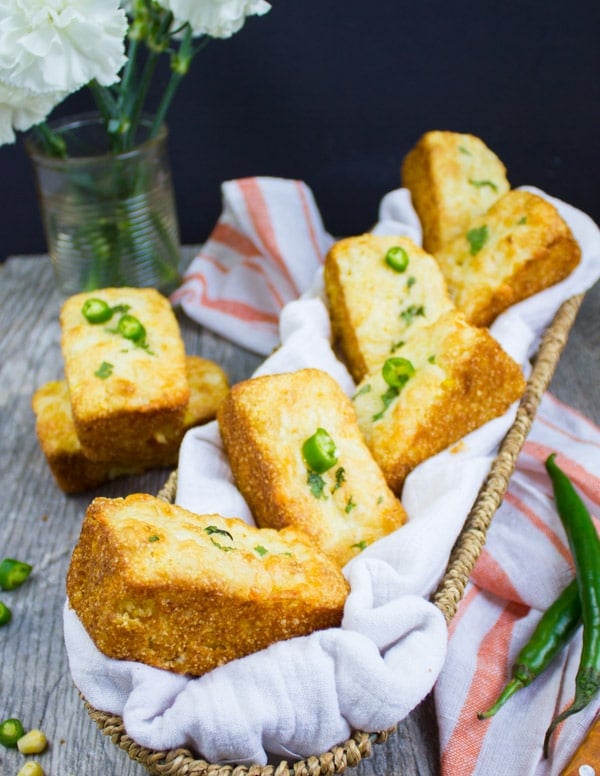 A basket with a few cornbread muffins and some spicy green chillies and a kitchen towel