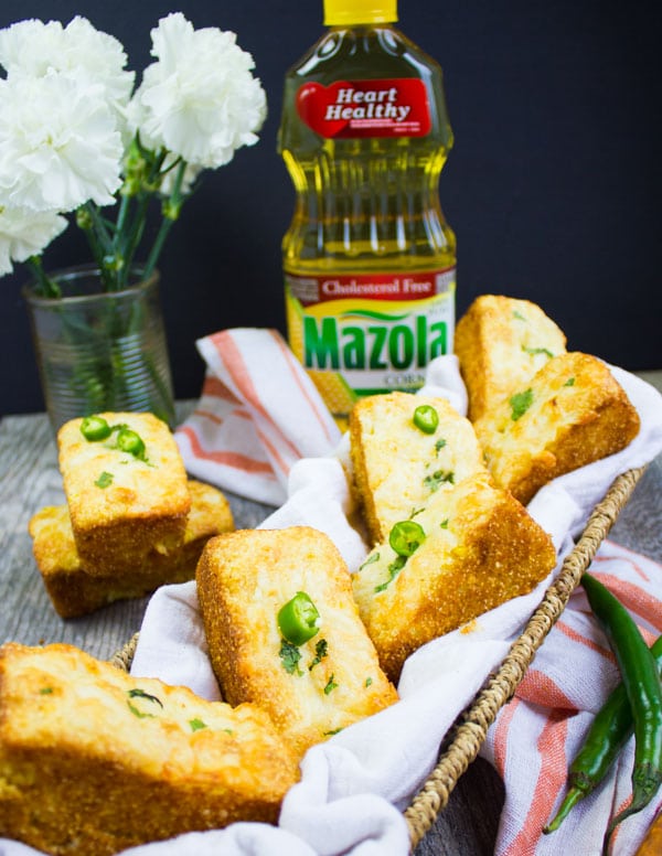 A huge basket with cornbread muffins and a bottle of mazola oil and a kitchen towel around