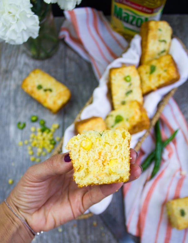 A hand holding a piece of cornbread muffin cut up to show the texture inside