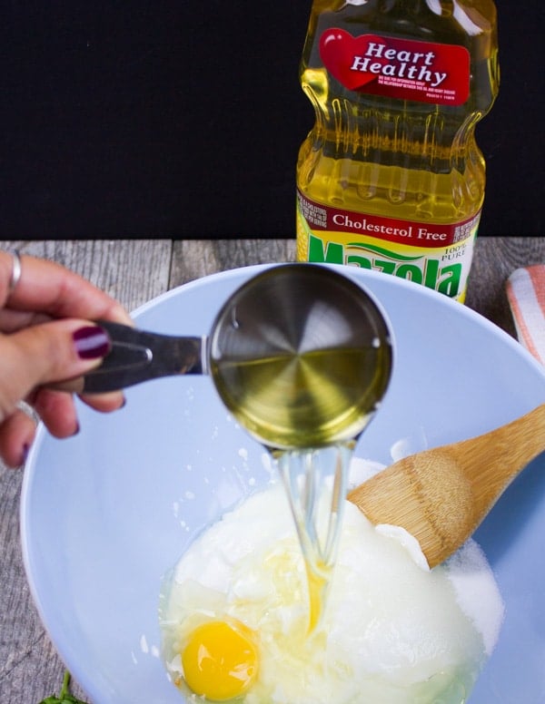 A cup pouring a quarter cup of oil over the bater to prepare the corn muffins