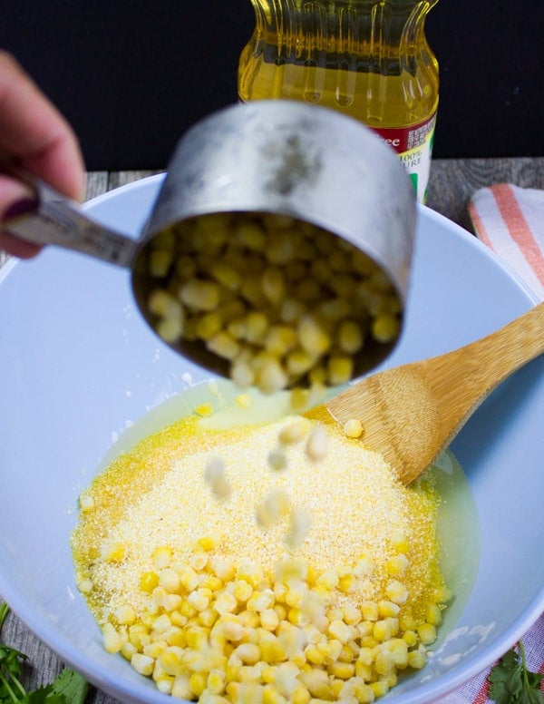 A bowl with the batter and a hand pouring in the fresh corn kernels into the batter