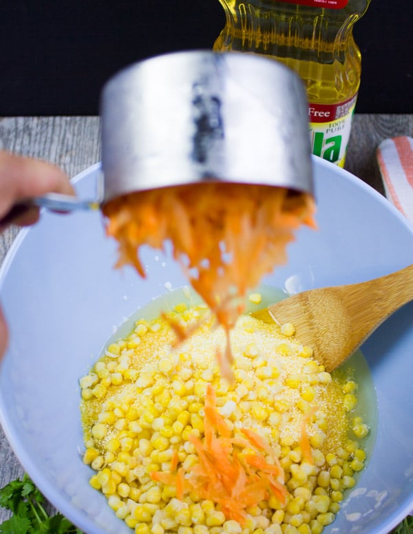 A hand pouring grated carrots over the corn bread batter