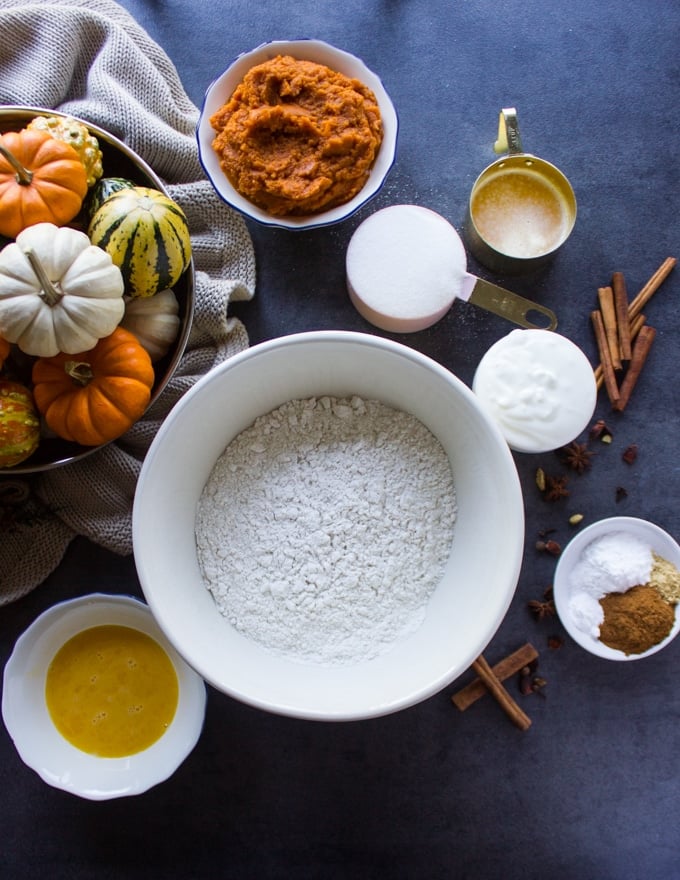 Ingredients for the pumpkin donuts a flour bowl, a spice bowl, melted butter, eggs, spice, sugar, yogurt and pumpkin puree