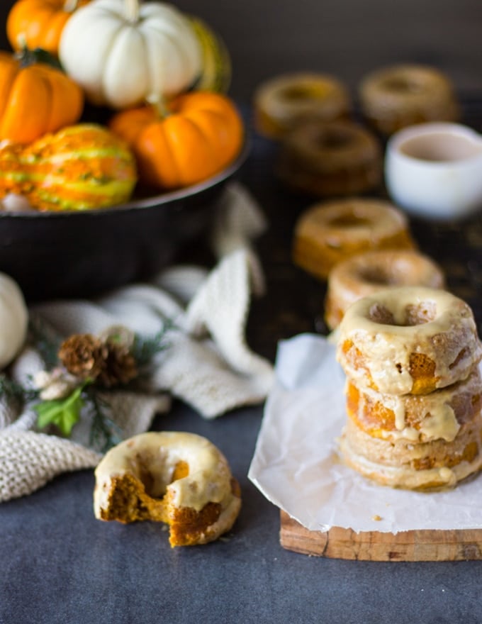 A bitten baked pumpkin donut on a surface with extra stacked pumpkin donuts in the background