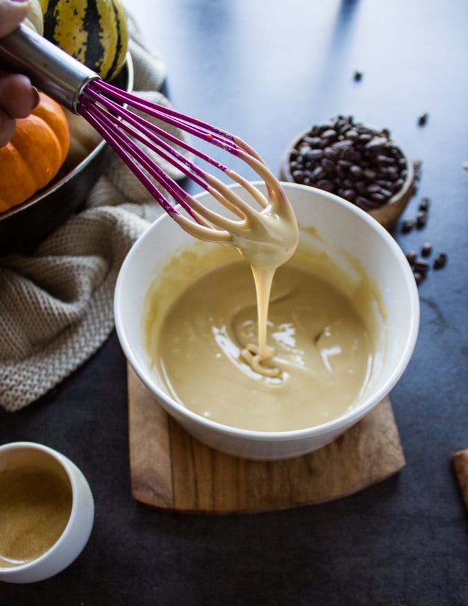 a whisk dripping some ready glaze over the bowl of glaze showing the thickness and consistency of the glaze