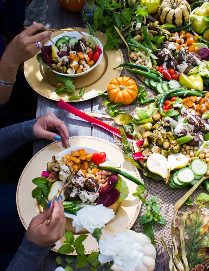 A table scape with pumpkin and fall decor and two bowls showing lamb meatballs, roast veggies and tahini sauce