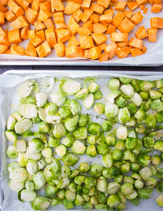 two baking sheets, one with cubes sweet potatoes and the other with Brussel Sprouts ready for roasting