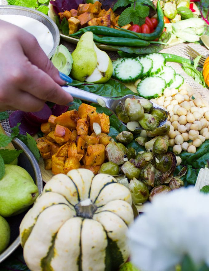 A bowl with some ingredients and a hand holding a spoon adding the remaining Brussel sprouts to the bowl.