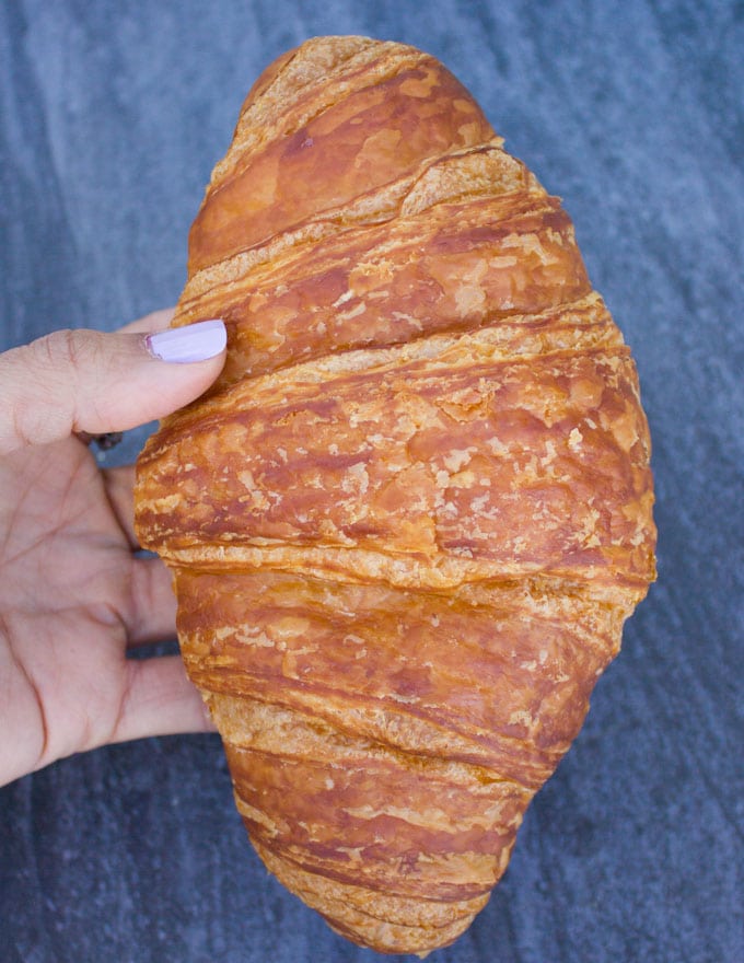 A hand holding a whole croissant