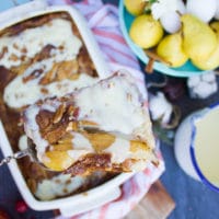 A spatula with a slice of croissant bread pudding elevated over the dish with pudding