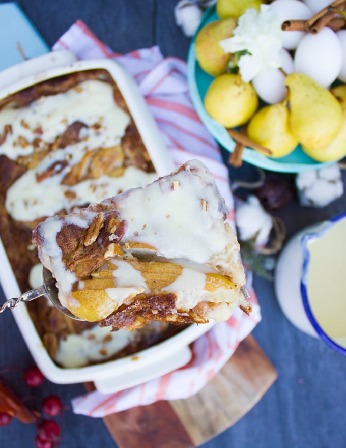 A spatula with a slice of croissant bread pudding elevated over the dish with pudding