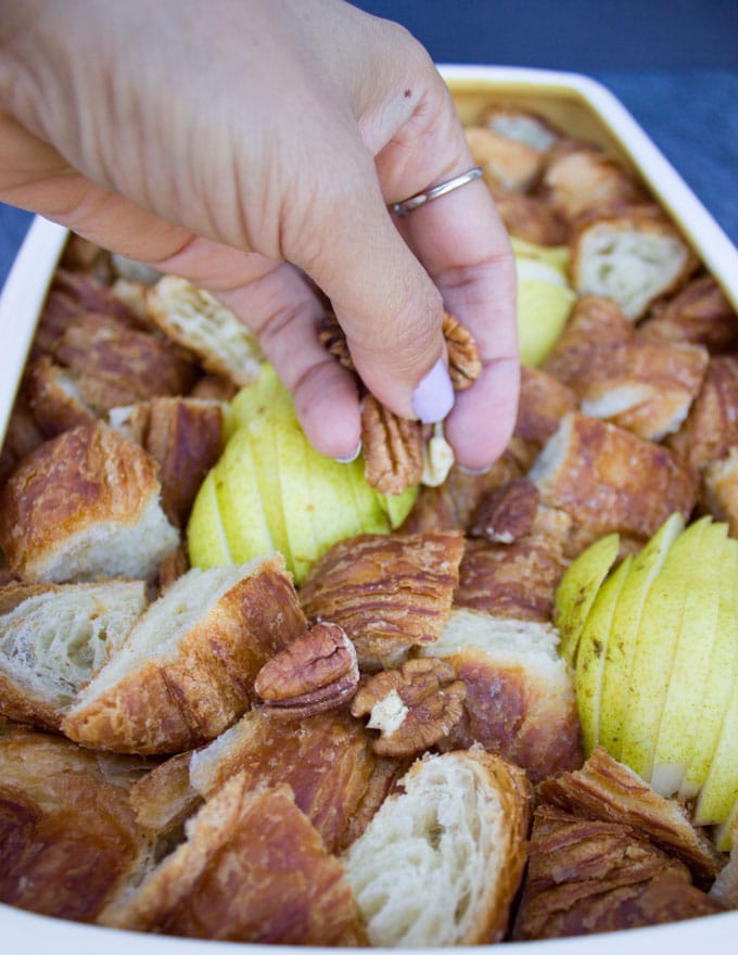 hand sprinkling some pecans over the croissant and pears