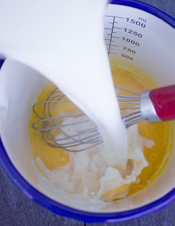 hot milk is poured over the egg yolk and sugar mixture with a whisk