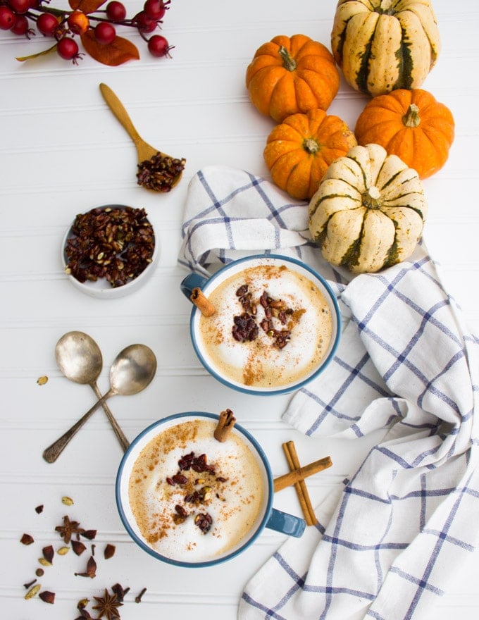 2 bowls of pumpkin spice oatmeal latte on a table with a table cloth and two spoons and some pumpkins