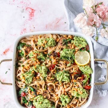 A large plate of broccoli pesto pasta with lemon slices as a garnish, some toasted pine nuts on top and parmesan cheese