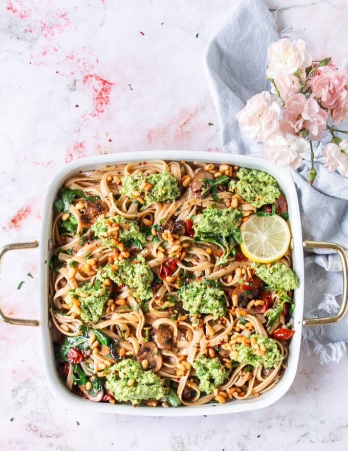 A large plate of broccoli pesto pasta with lemon slices as a garnish, some toasted pine nuts on top and parmesan cheese
