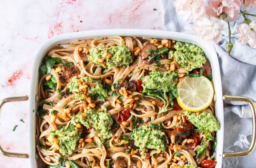 A large plate of broccoli pesto pasta with lemon slices as a garnish, some toasted pine nuts on top and parmesan cheese