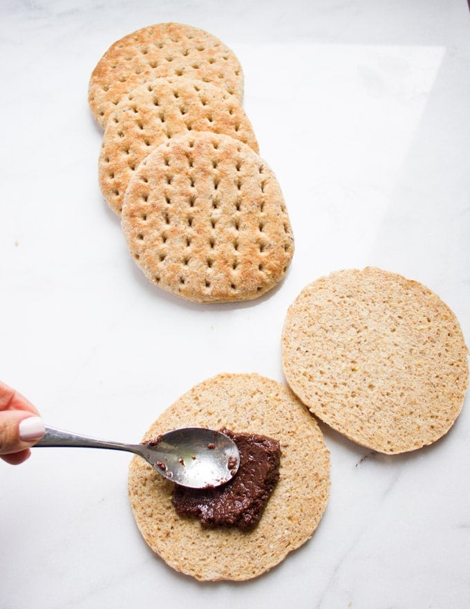 A hand spreading a black olive tapenade over the bottom of a whole wheat pita bun