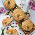 Top view of a white granite with a wooden board and turkey sandwiches over the wooden board. Another cut sandwich on the sandwich and flowers. Green chillies next to the cut up sandwich.