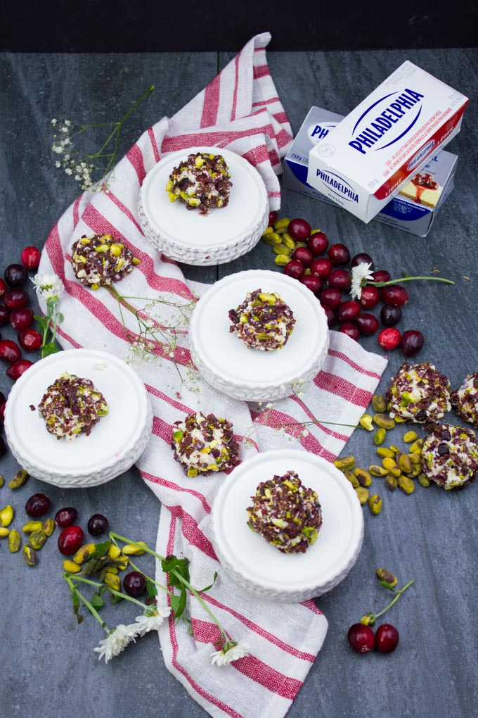 A series of mini cheesecake bites scattered over a kitchen towel with crushed pistachios and cranberries