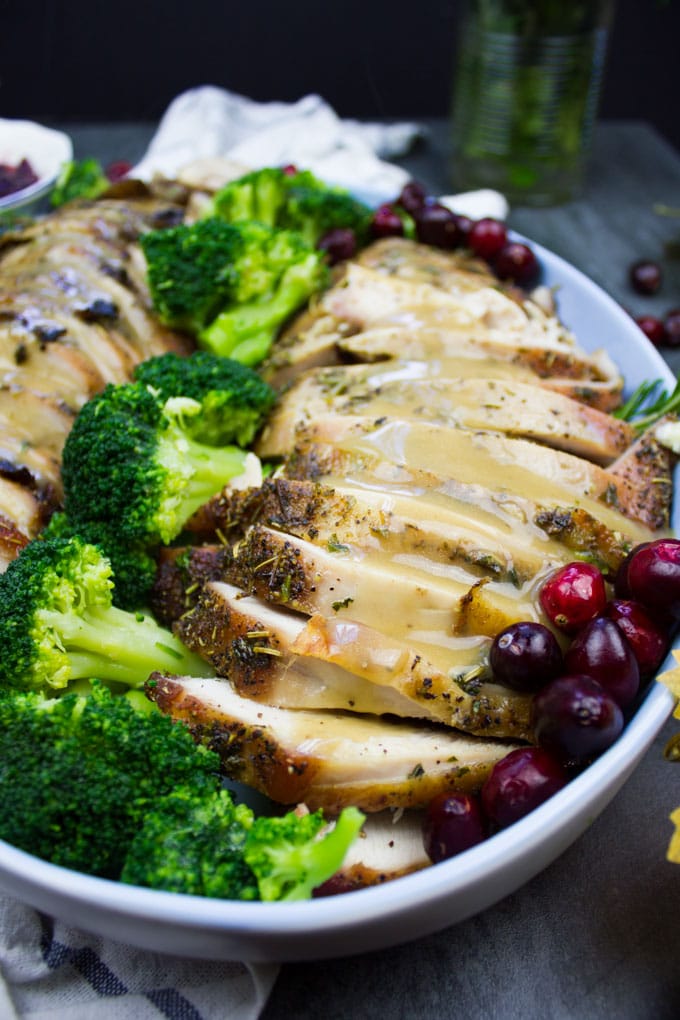 Close up of the finished sliced turkey breasts on a platter with some broccoli and fresh cranberries