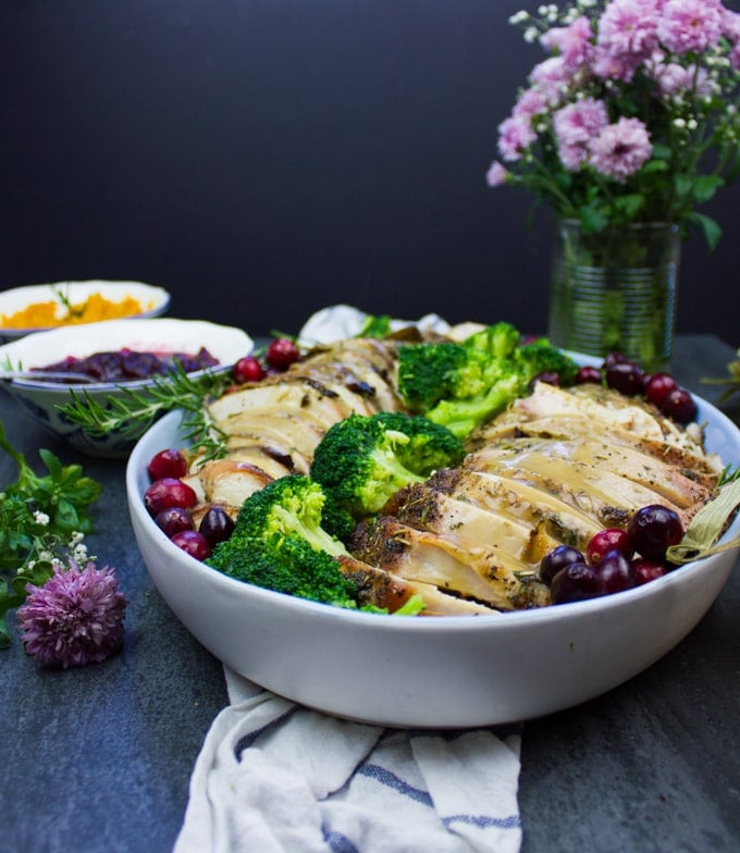 A side view of a platter showing some sliced roasted dry brined turkey breast with gravy drizzled on top.