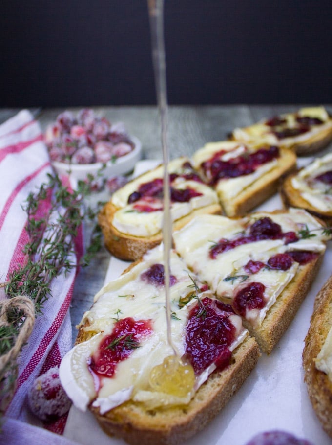 Honey being drizzled over a baked brie toast right out of the oven with cranberries