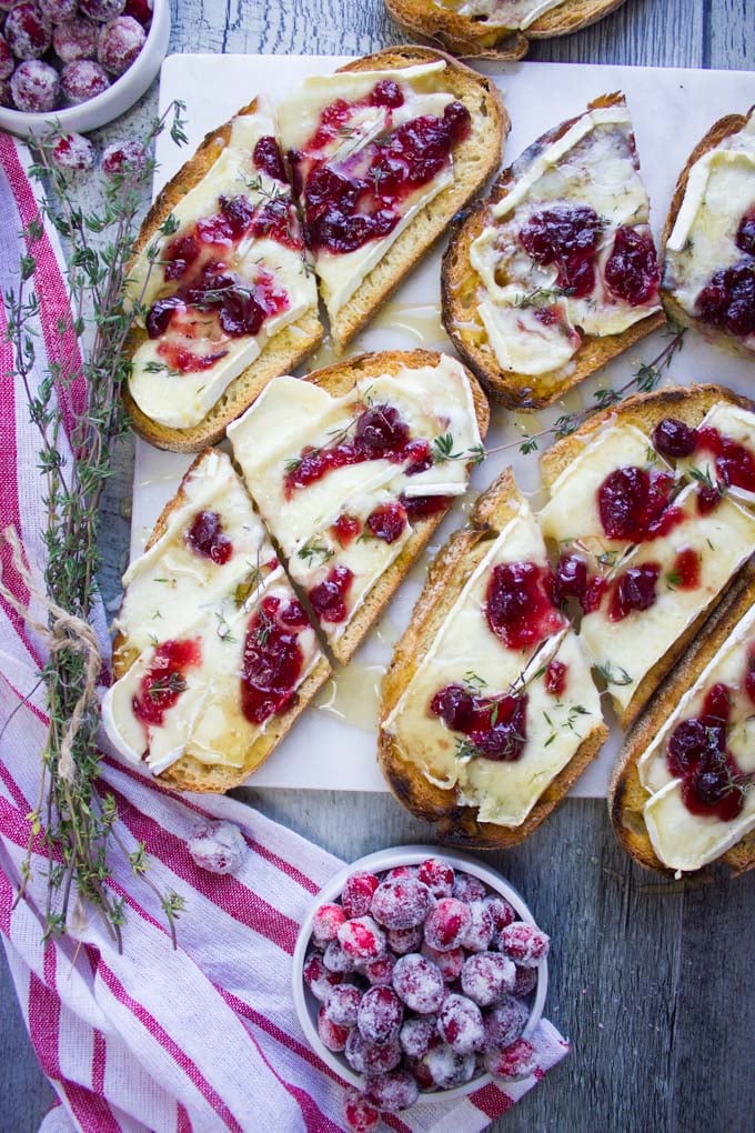 Top view and close up of two baked brie toats with cranberries and drenched in a honey drizzle